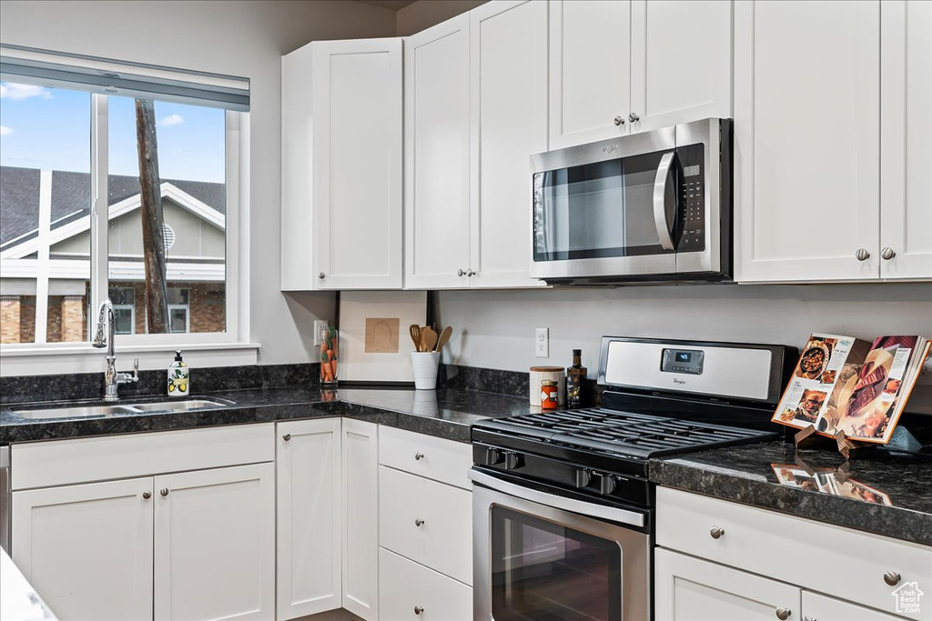 Kitchen featuring sink, dark stone counters, white cabinetry, and stainless steel appliances