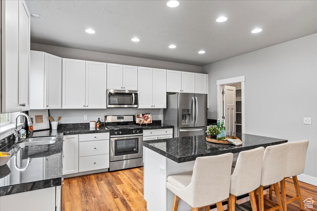 Kitchen with white cabinets, a kitchen island, light wood-type flooring, stainless steel appliances, and a kitchen bar