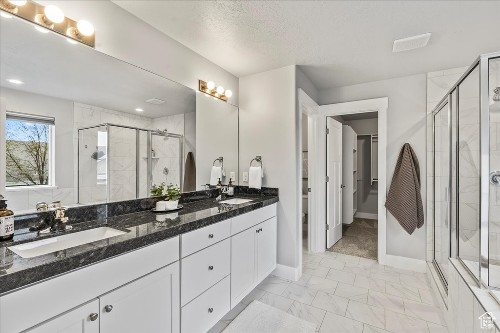 Bathroom with a textured ceiling, dual vanity, tile flooring, and walk in shower