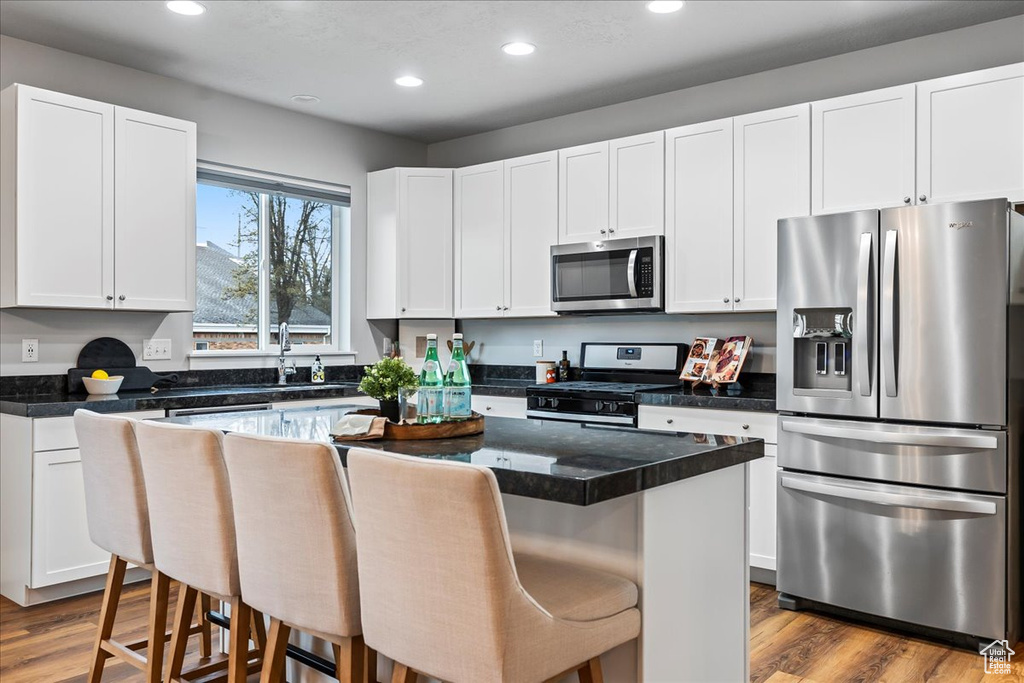 Kitchen featuring a kitchen breakfast bar, white cabinets, stainless steel appliances, and light hardwood / wood-style flooring