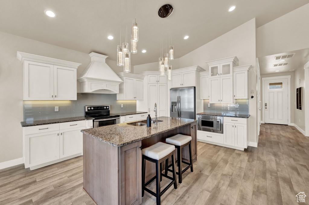 Kitchen with premium range hood, light wood-type flooring, appliances with stainless steel finishes, and backsplash