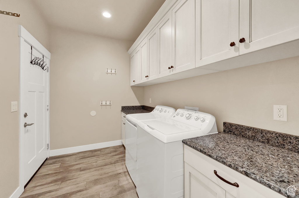 Laundry room featuring washing machine and dryer, light hardwood / wood-style flooring, and cabinets