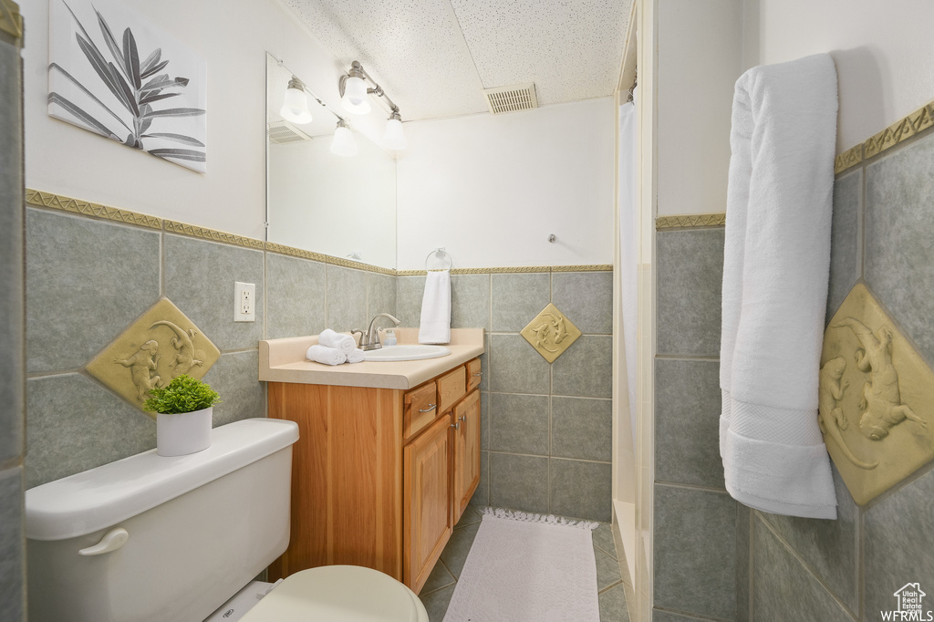 Bathroom featuring a textured ceiling, vanity, tile walls, and toilet