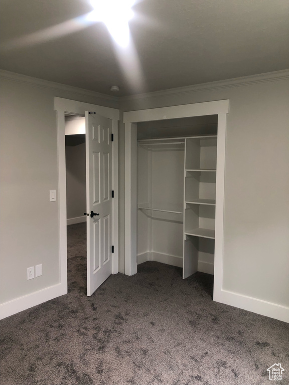 Unfurnished bedroom featuring dark carpet, a closet, and crown molding