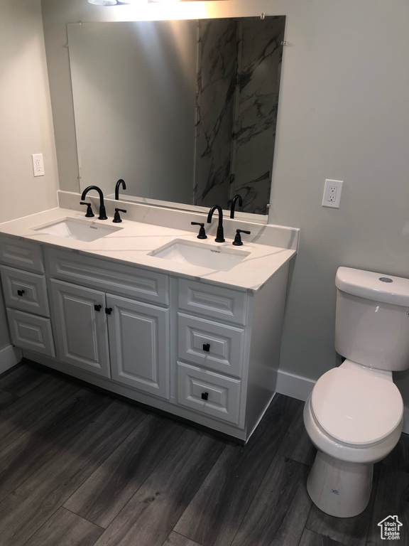 Bathroom featuring dual bowl vanity, toilet, and wood-type flooring