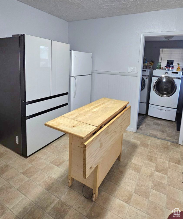 Kitchen with separate washer and dryer, a textured ceiling, white refrigerator, and light tile flooring