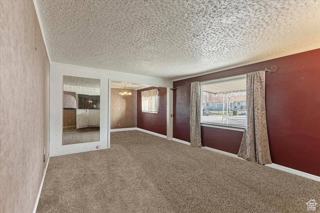 Unfurnished room featuring a notable chandelier, dark carpet, and a textured ceiling