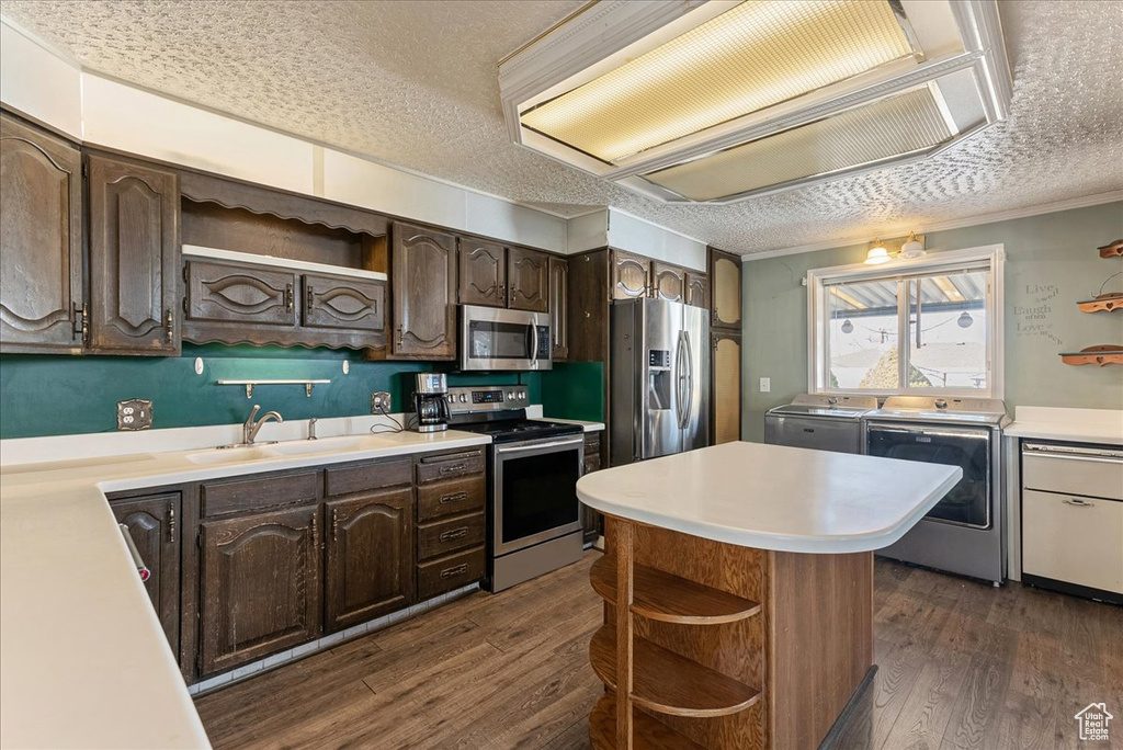 Kitchen with appliances with stainless steel finishes, dark hardwood / wood-style floors, washing machine and clothes dryer, a textured ceiling, and dark brown cabinets