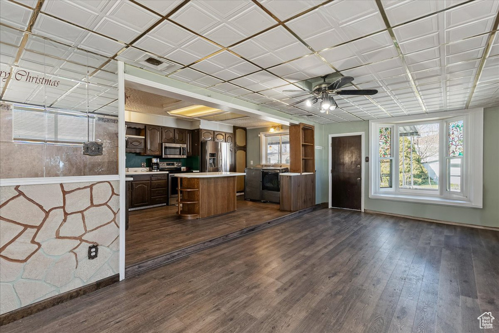 Kitchen with ceiling fan, appliances with stainless steel finishes, dark hardwood / wood-style flooring, a center island, and dark brown cabinets