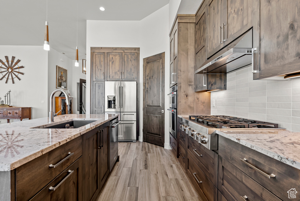 Kitchen featuring backsplash, light hardwood / wood-style flooring, sink, appliances with stainless steel finishes, and hanging light fixtures