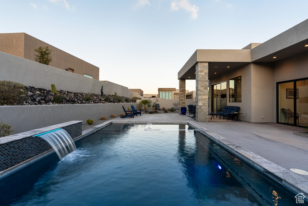 Pool at dusk featuring a patio area and pool water feature