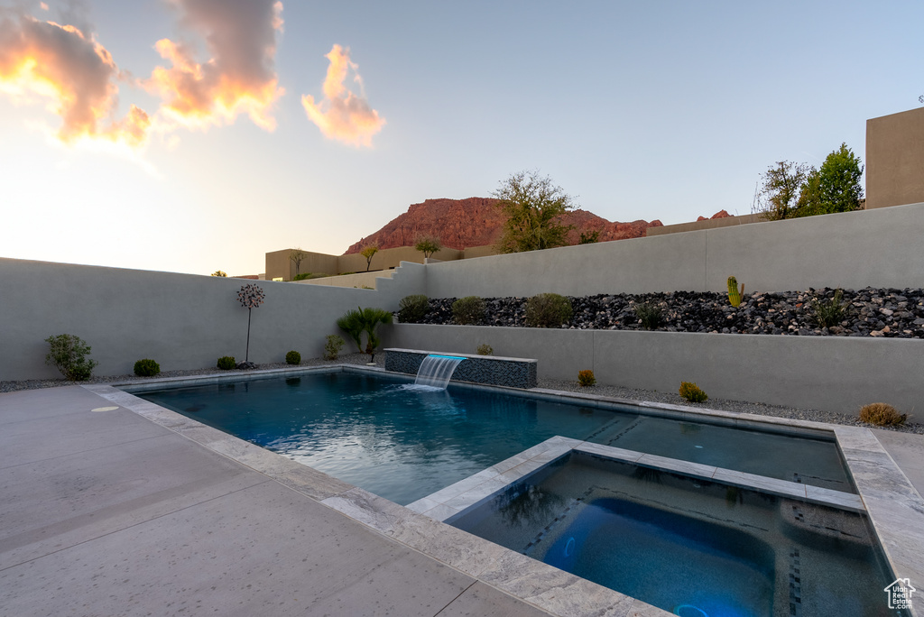 Pool at dusk with an in ground hot tub, pool water feature, and a patio area