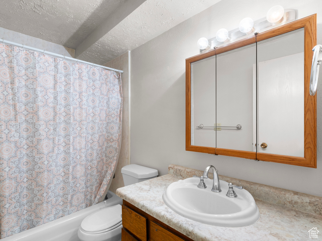 Full bathroom with shower / bath combo, vanity, toilet, and a textured ceiling