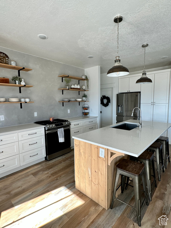 Kitchen featuring stainless steel appliances, decorative light fixtures, light hardwood / wood-style flooring, white cabinets, and a kitchen island with sink