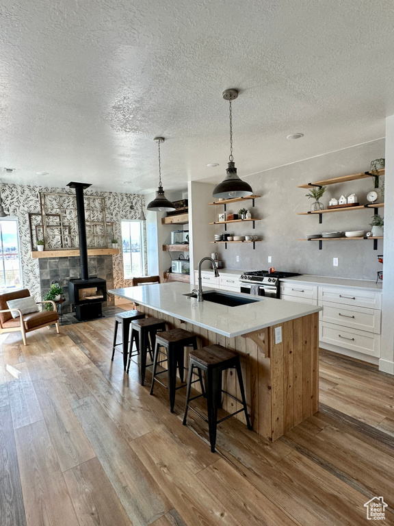 Kitchen featuring light hardwood / wood-style floors, a textured ceiling, white cabinets, a wood stove, and sink