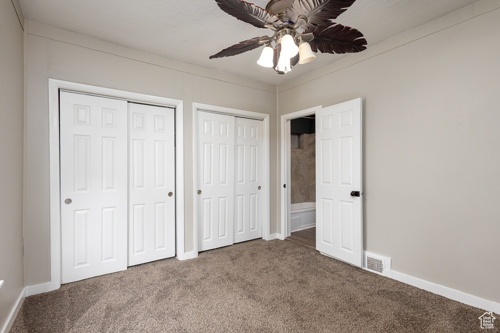 Unfurnished bedroom with dark carpet, multiple closets, and ceiling fan