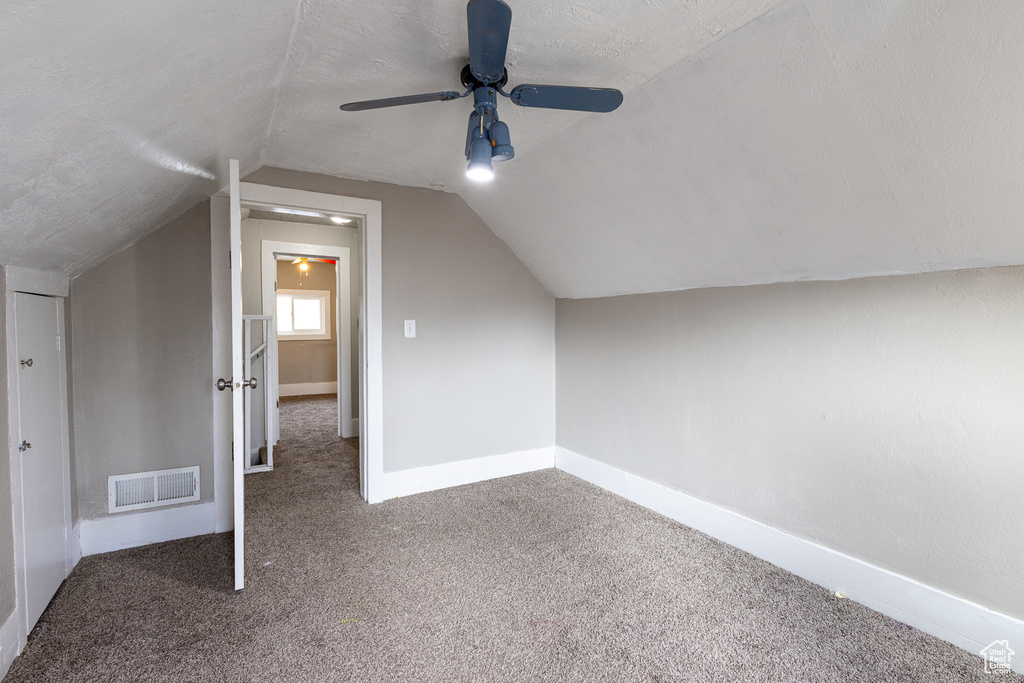 Additional living space with a textured ceiling, dark colored carpet, vaulted ceiling, and ceiling fan