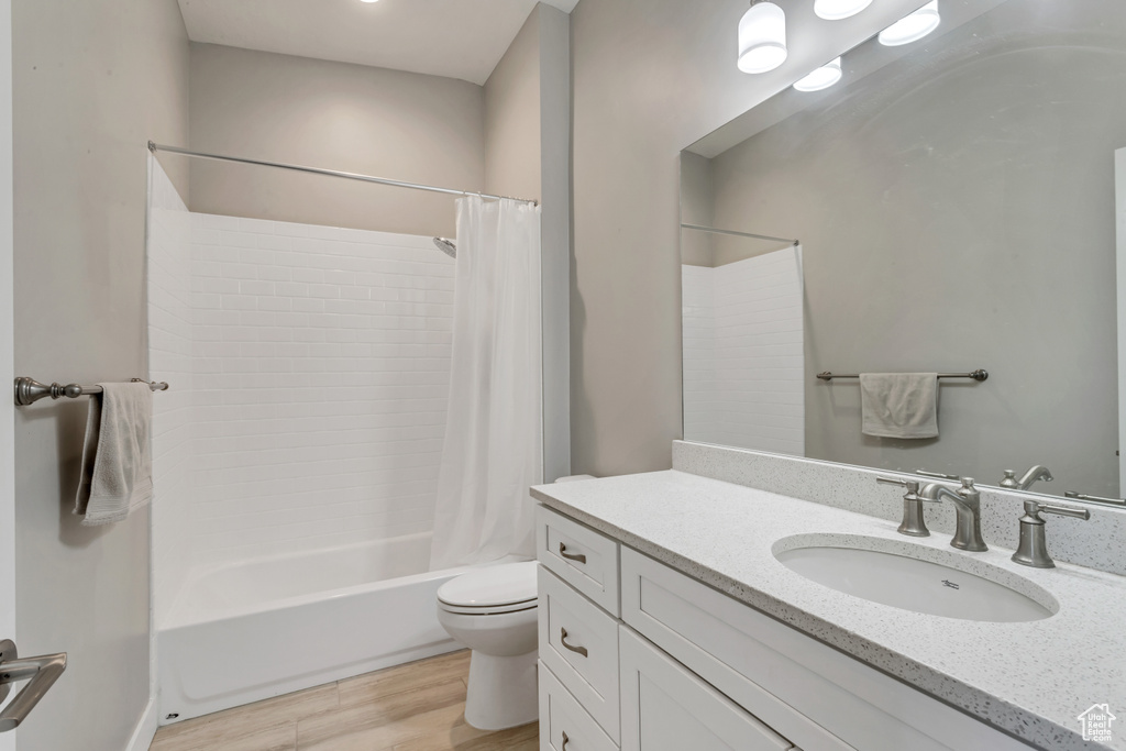 Full bathroom with wood-type flooring, shower / bathtub combination with curtain, large vanity, and toilet