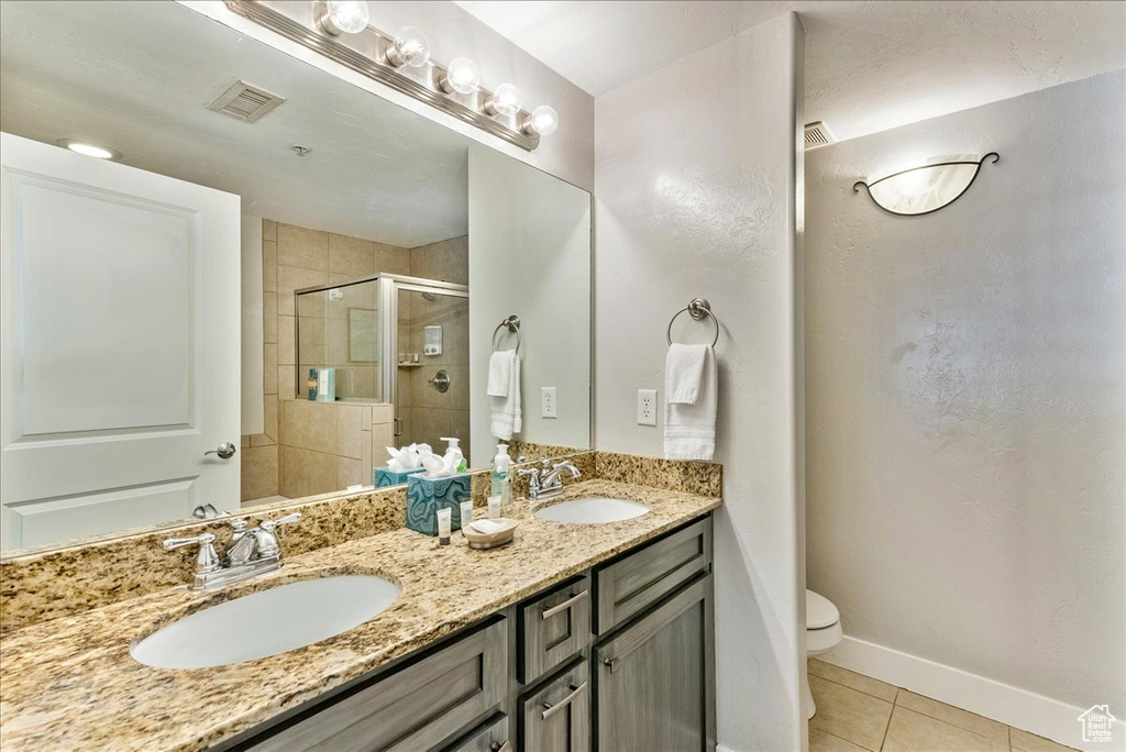 Bathroom with dual sinks, tile flooring, large vanity, an enclosed shower, and toilet