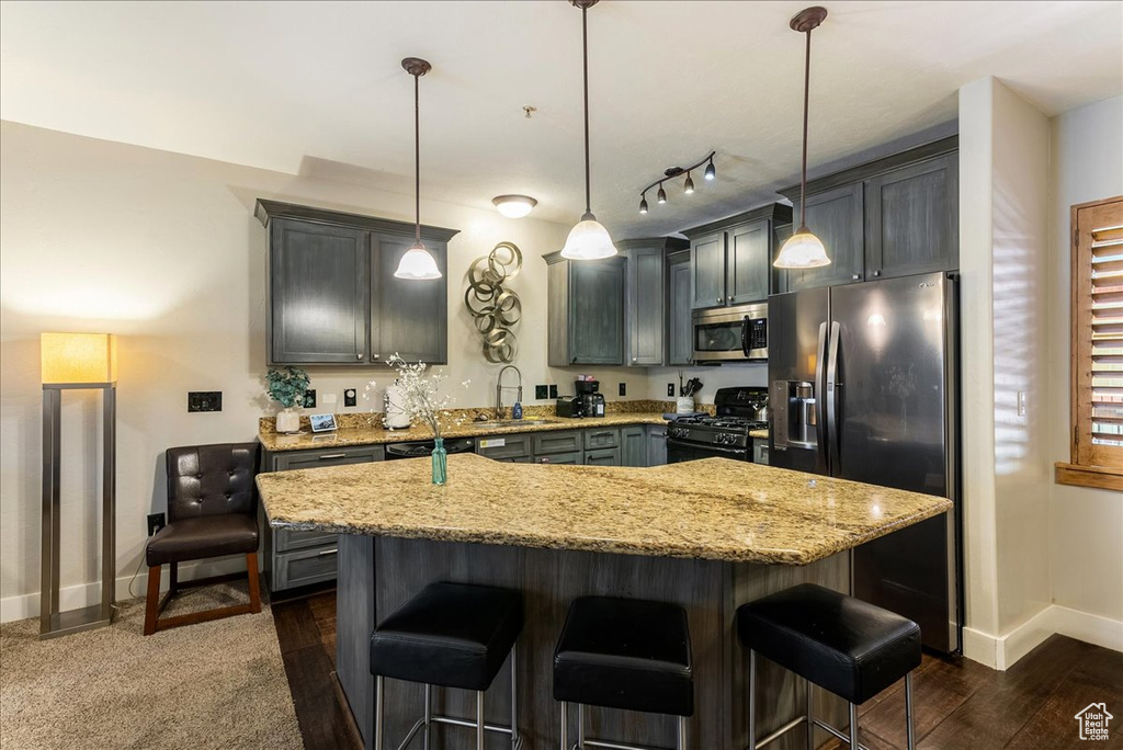 Kitchen featuring appliances with stainless steel finishes, a center island, light stone countertops, and decorative light fixtures