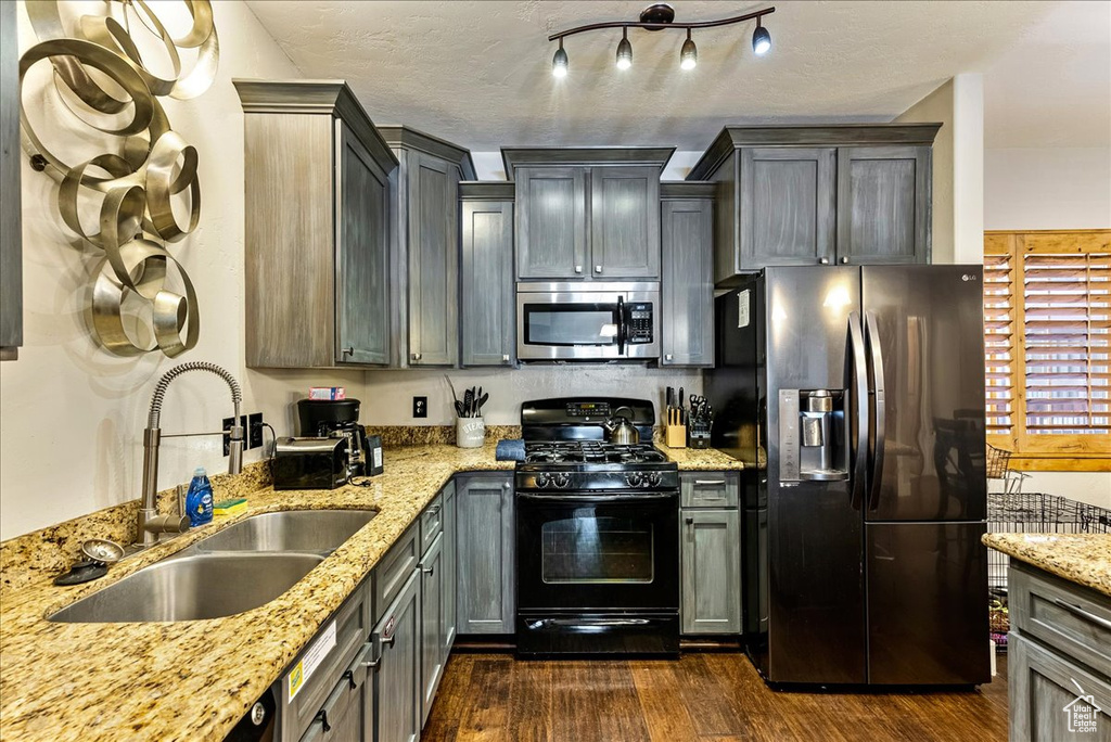 Kitchen featuring light stone countertops, refrigerator with ice dispenser, sink, and black range with gas cooktop