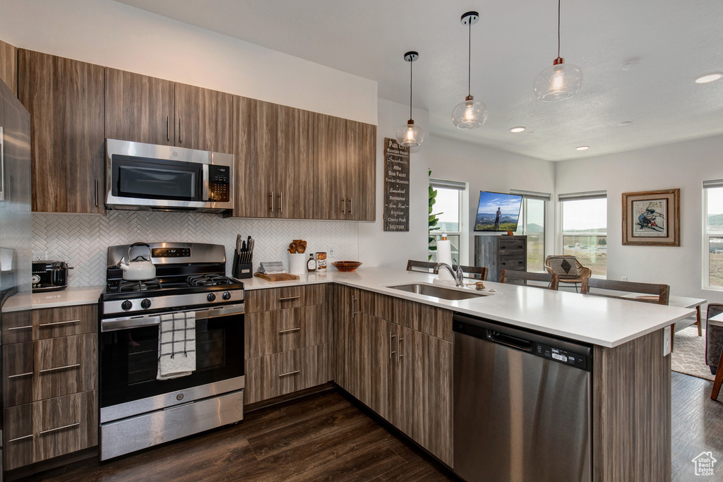 Kitchen with stainless steel appliances, decorative light fixtures, tasteful backsplash, dark hardwood / wood-style floors, and kitchen peninsula
