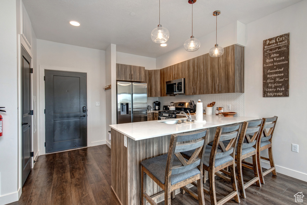 Kitchen with dark hardwood / wood-style flooring, a breakfast bar, appliances with stainless steel finishes, and kitchen peninsula