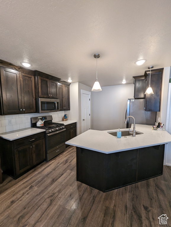 Kitchen with backsplash, appliances with stainless steel finishes, sink, hanging light fixtures, and dark wood-type flooring