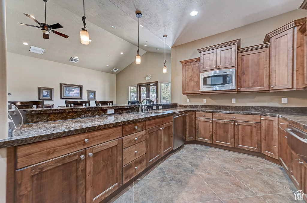 Kitchen with ceiling fan, pendant lighting, stainless steel appliances, dark stone counters, and light tile floors