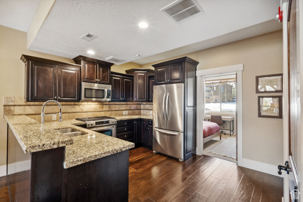 Kitchen with backsplash, appliances with stainless steel finishes, kitchen peninsula, and dark hardwood / wood-style floors