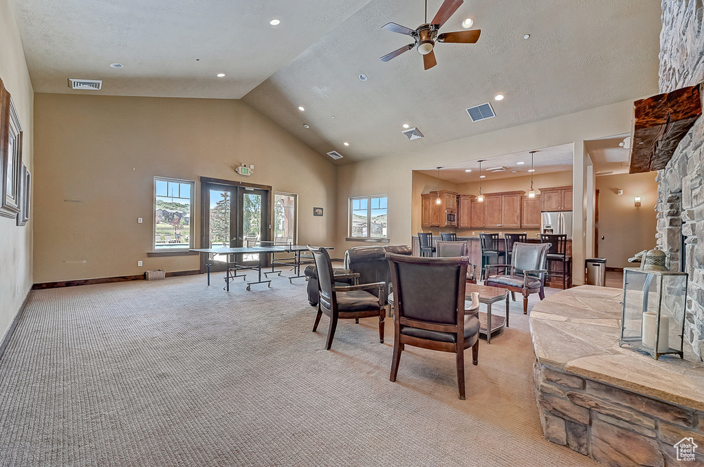 Living room featuring ceiling fan, high vaulted ceiling, a stone fireplace, a textured ceiling, and light colored carpet