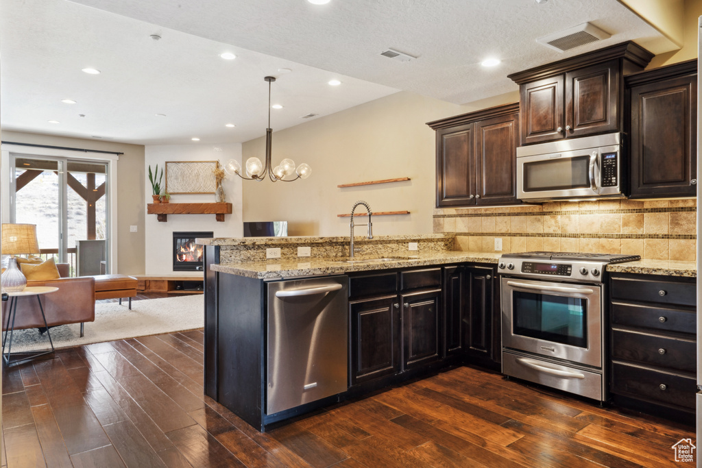Kitchen featuring appliances with stainless steel finishes, light stone counters, a chandelier, and dark hardwood / wood-style flooring