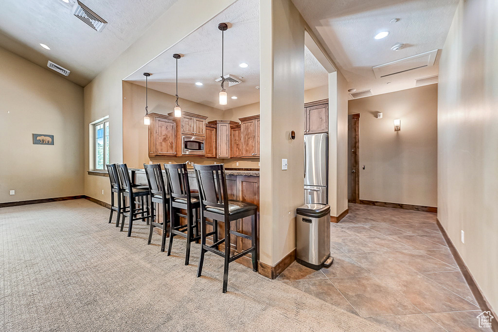 Kitchen featuring pendant lighting, kitchen peninsula, stainless steel appliances, light colored carpet, and a kitchen bar