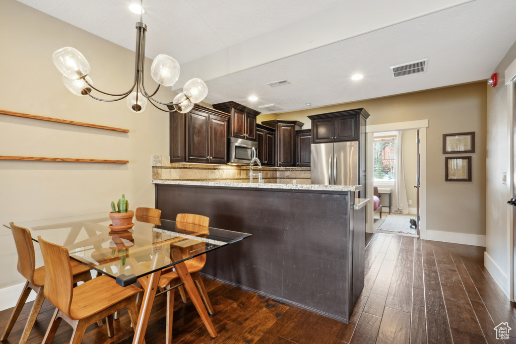 Kitchen with hanging light fixtures, light stone counters, stainless steel appliances, a chandelier, and dark wood-type flooring
