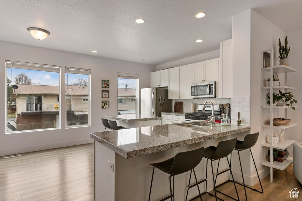Kitchen featuring white cabinetry, a kitchen bar, stainless steel appliances, and light hardwood / wood-style flooring