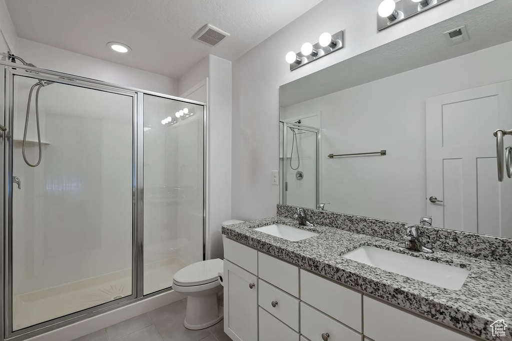 Bathroom featuring a shower with shower door, tile flooring, oversized vanity, toilet, and double sink
