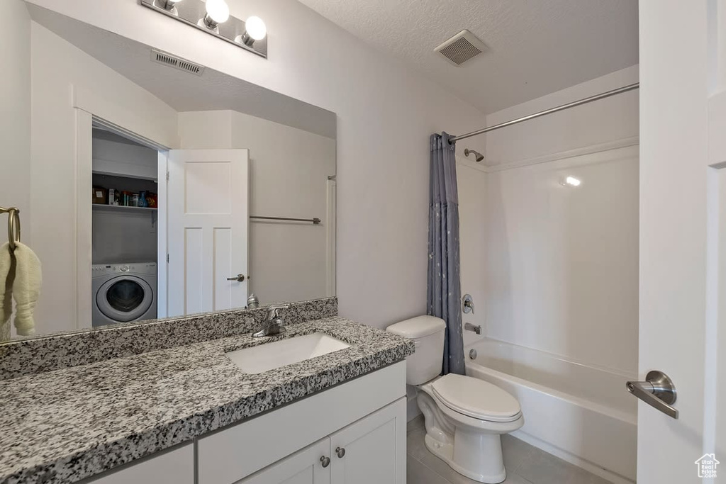 Full bathroom with washer / dryer, tile floors, oversized vanity, toilet, and shower / bath combo