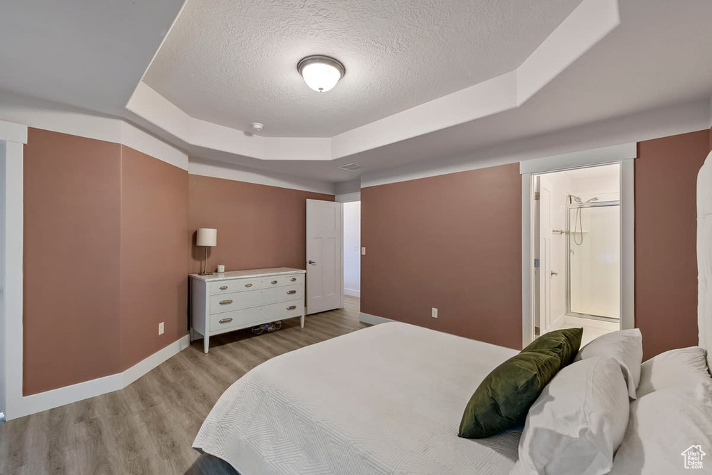 Bedroom featuring light wood-type flooring, a tray ceiling, a textured ceiling, and connected bathroom