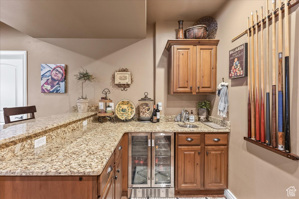 Kitchen featuring light stone countertops, sink, wine cooler, and kitchen peninsula