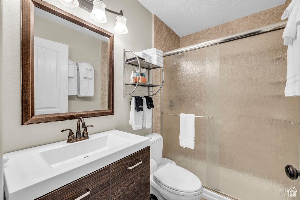Bathroom with a textured ceiling, an enclosed shower, vanity, and toilet