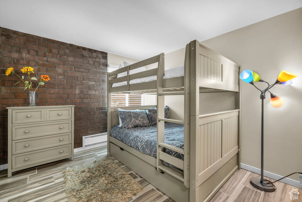 Bedroom with light hardwood / wood-style floors, a baseboard radiator, and brick wall