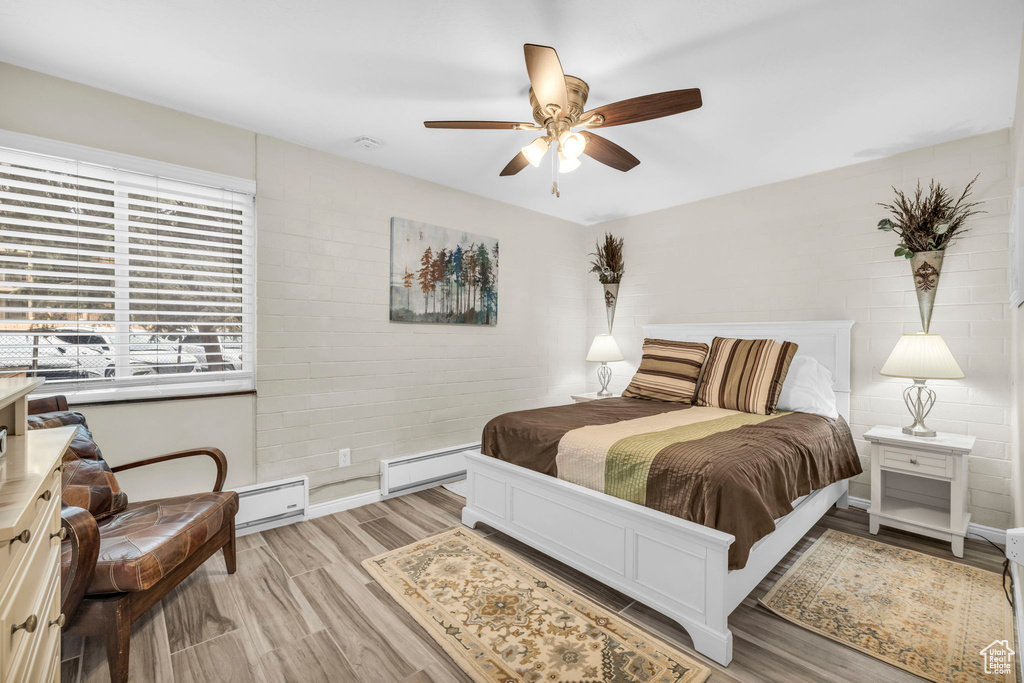 Bedroom with light hardwood / wood-style floors, baseboard heating, and ceiling fan