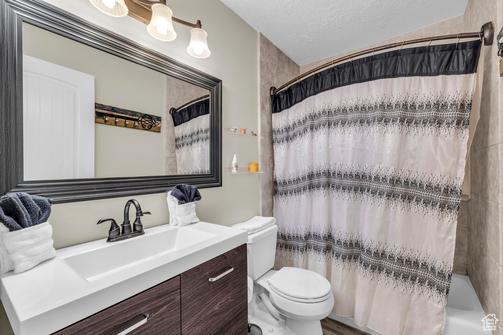 Full bathroom featuring vanity, shower / tub combo, toilet, and a textured ceiling
