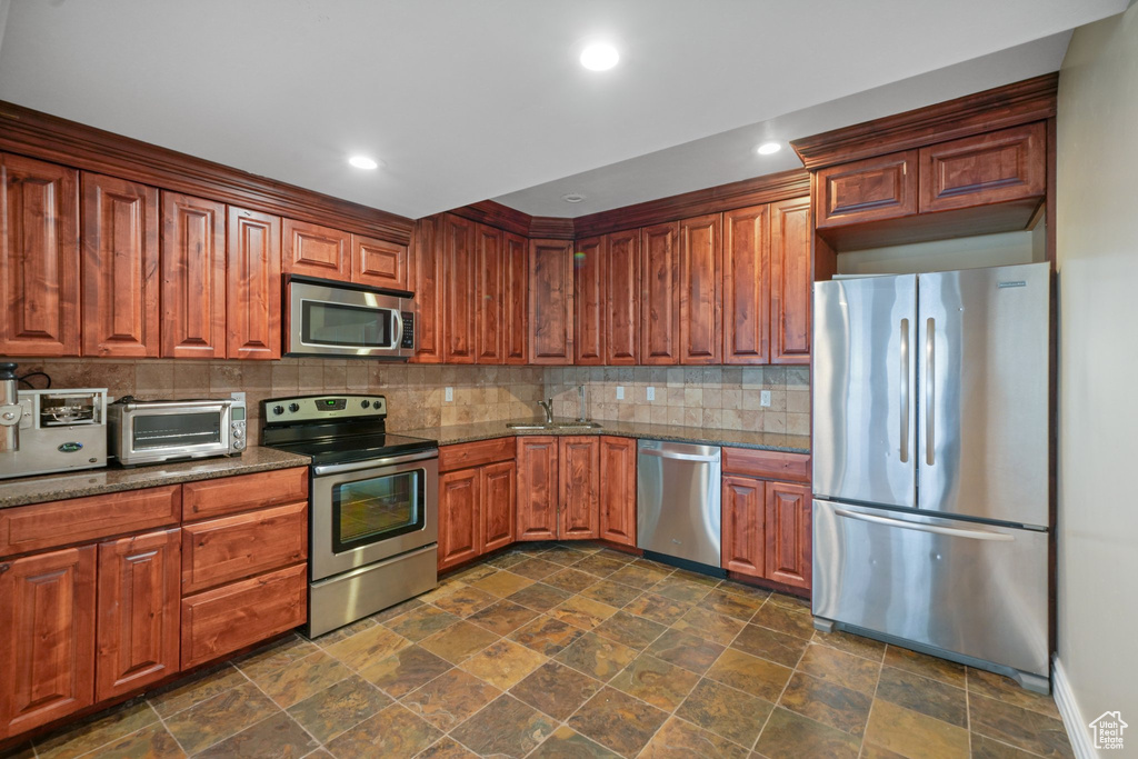 Kitchen featuring backsplash, sink, dark tile flooring, and stainless steel appliances
