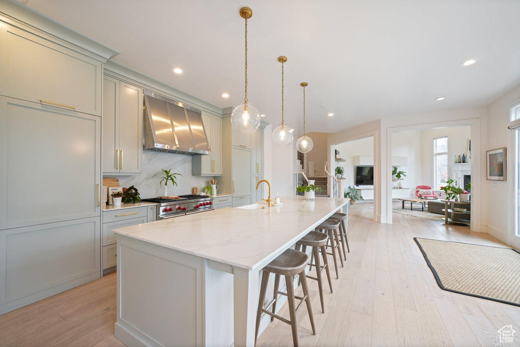 Kitchen featuring light hardwood / wood-style floors, light stone countertops, wall chimney range hood, pendant lighting, and high end range