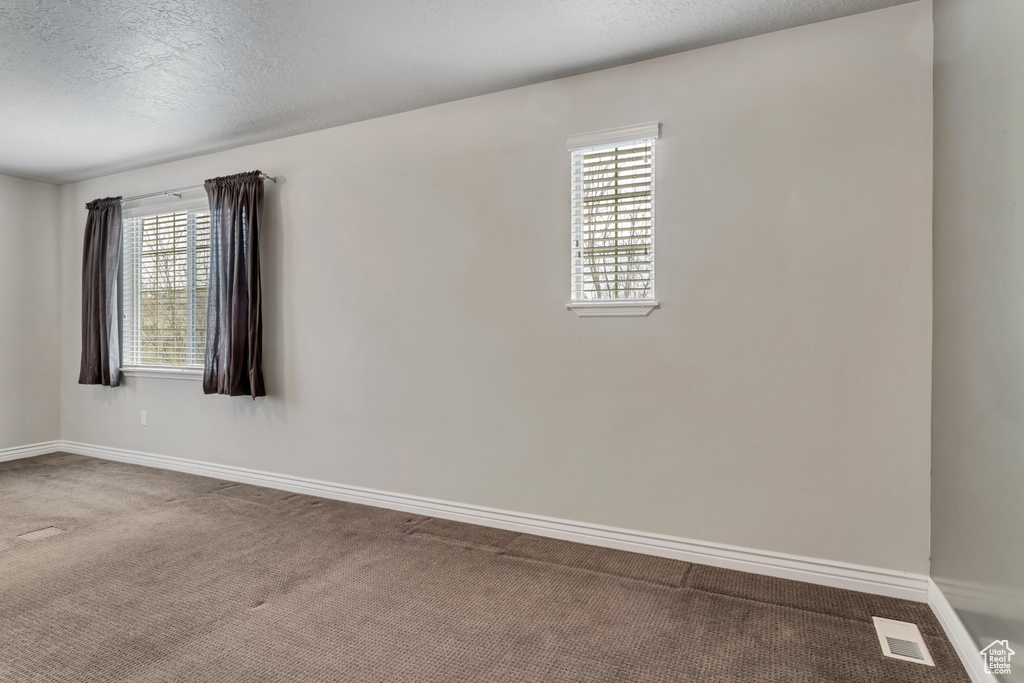 Spare room featuring plenty of natural light, dark colored carpet, and a textured ceiling