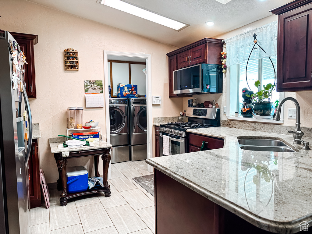Kitchen featuring washer and dryer, sink, light stone countertops, stainless steel appliances, and light tile flooring