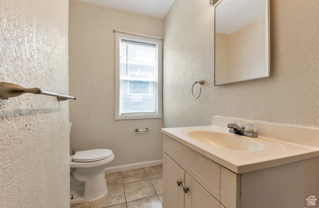 Bathroom with toilet, tile flooring, vanity with extensive cabinet space, and a healthy amount of sunlight