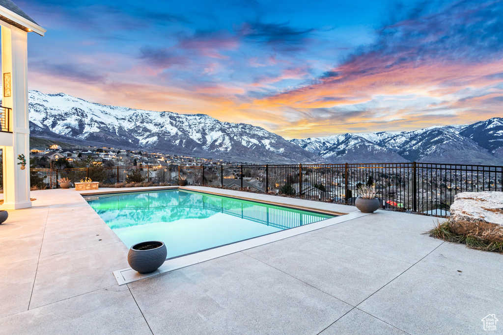 Pool at dusk featuring a mountain view and a patio area