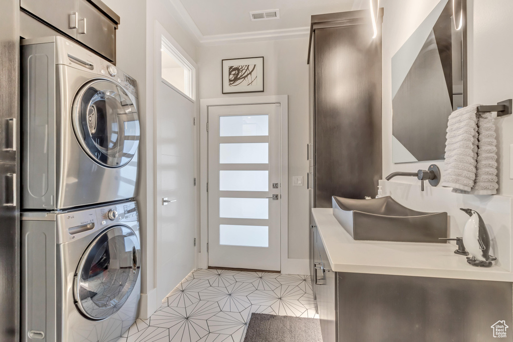 Laundry room featuring ornamental molding, stacked washer / drying machine, and light tile floors
